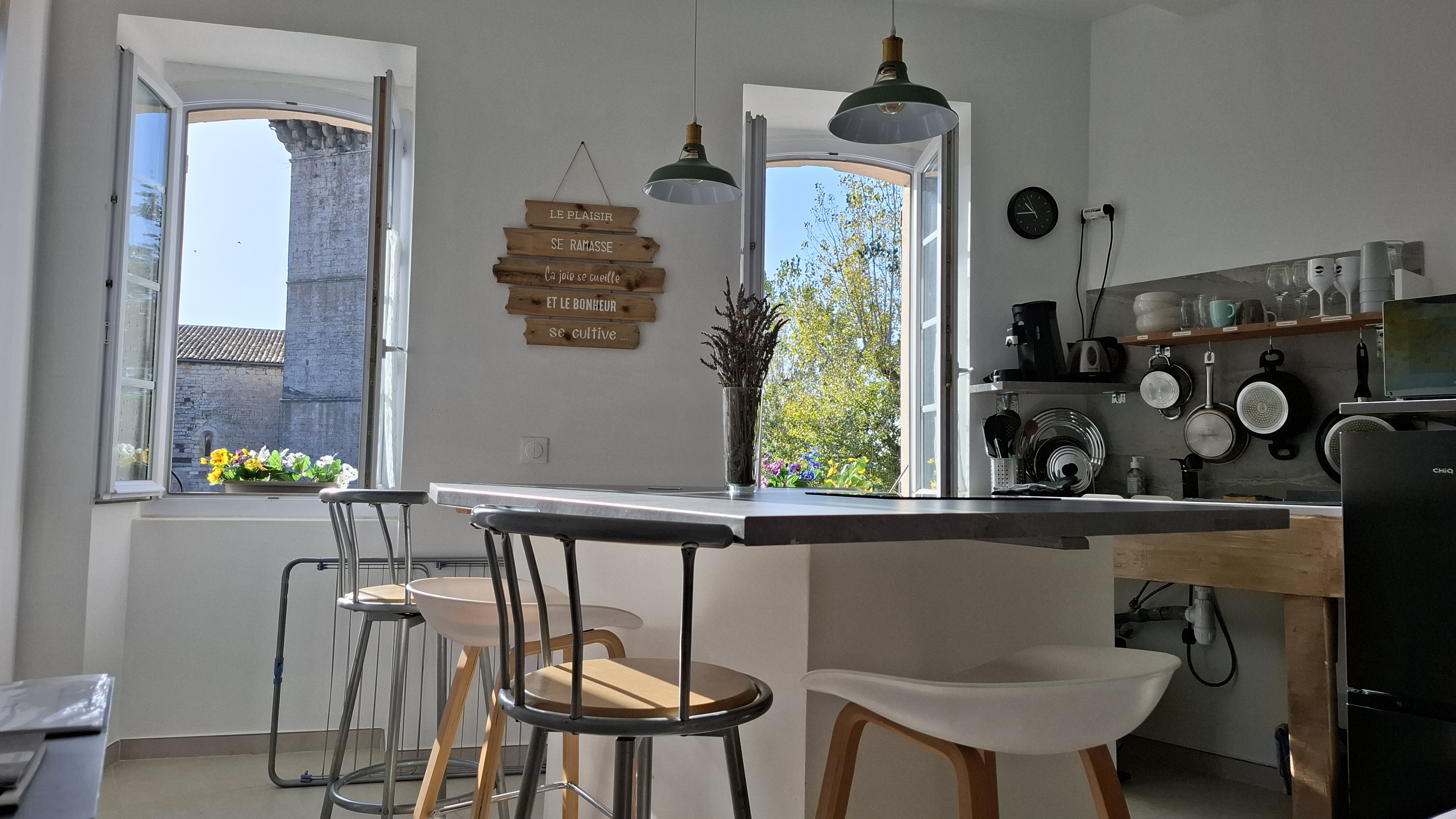 A kitchen with a wooden bar and two standing bar stools. The counter looks into a garden or patio.