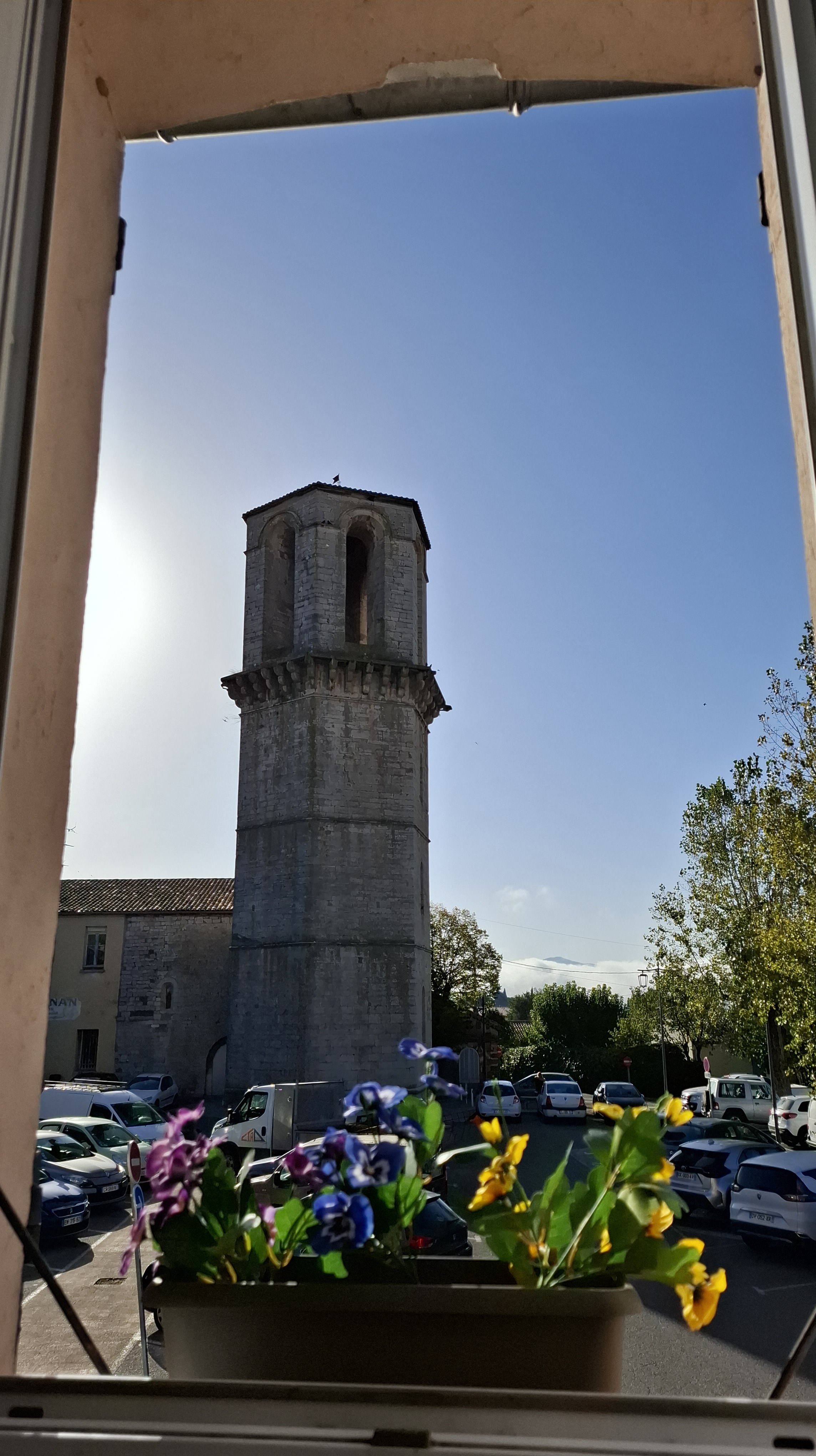 The building in the image appears to be a belfry with several cars and trees surrounding it.