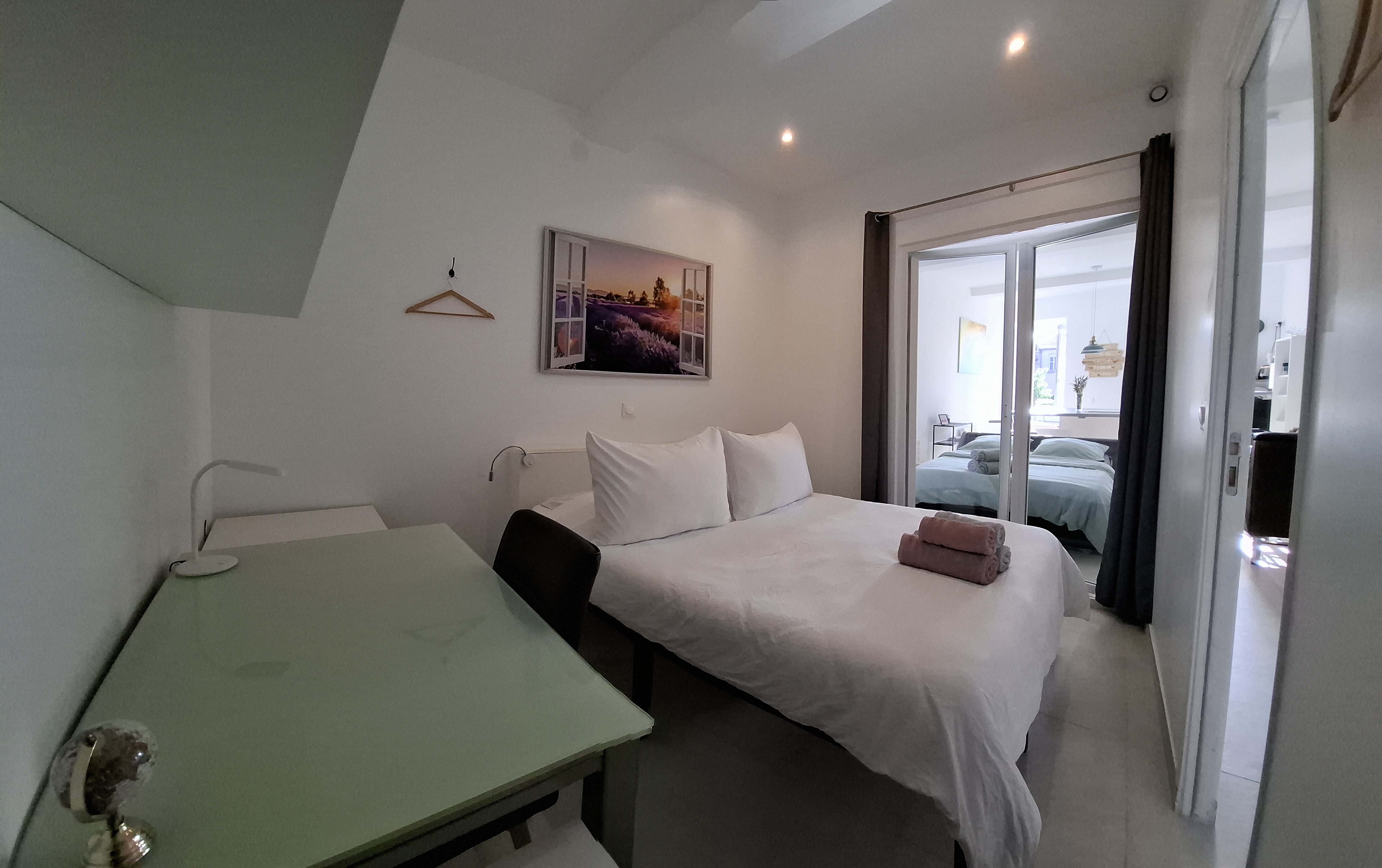 La chambre couvre le premier plan de la vue, équipée d'un lit simple avec de simples oreillers blanchis et deux odes rigol...