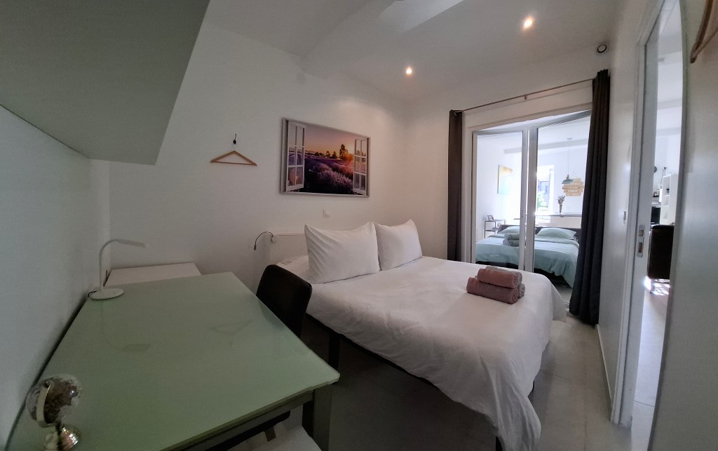 La chambre couvre le premier plan de la vue, équipée d'un lit simple avec de simples oreillers blanchis et deux odes rigol...